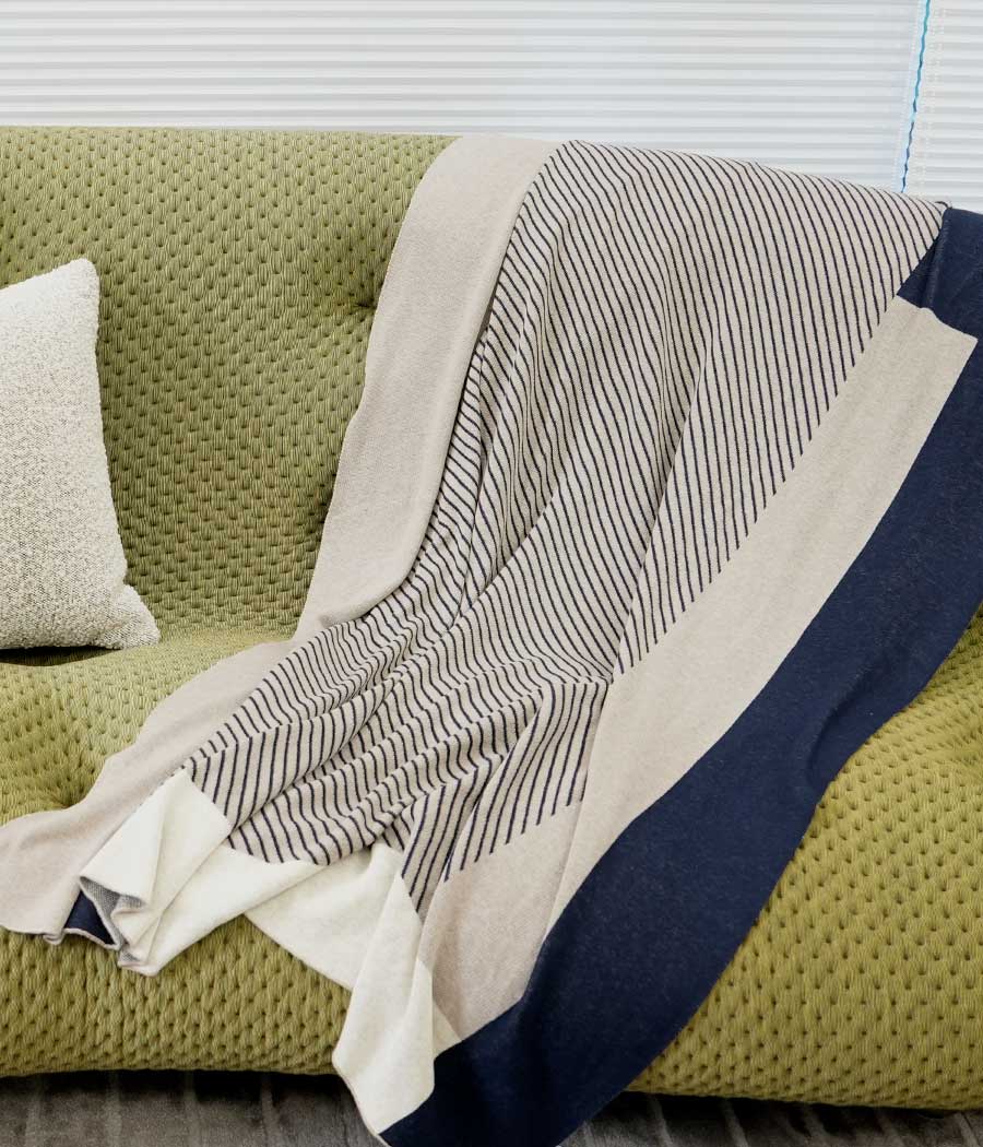 Wool blend throw blanket in dark teal with stripe patterns putting on sofa